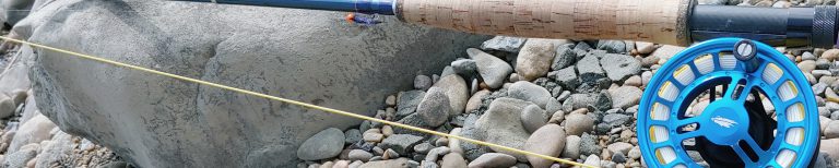 Reel Fly Fishers 6-weight versatile fly rod with chrono fly fishing reel leaning on a rock on a rocky beach